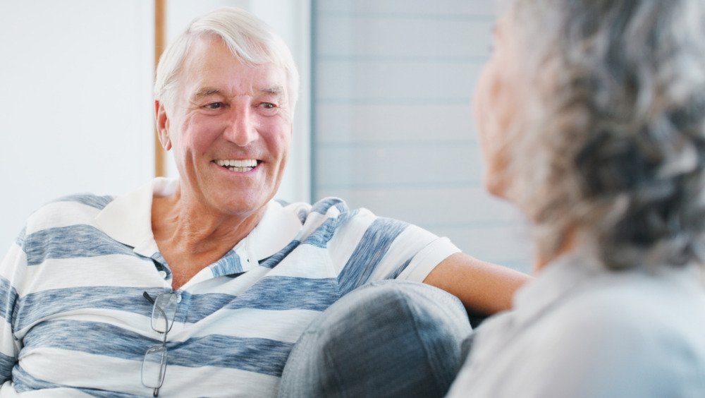 Senior couple, at home and happy on a sofa in the living room, in conversation.