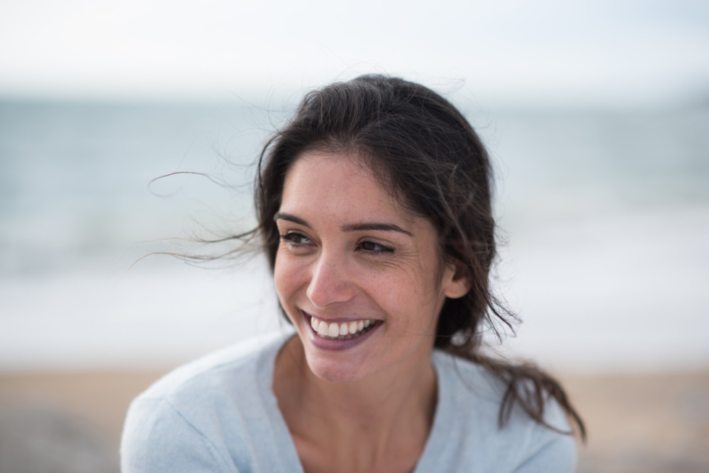 Closeup image of a young brunette woman smiling on the beach.