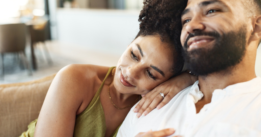 Happy couple relaxing on a sofa; the woman rests her head on the man's shoulder.