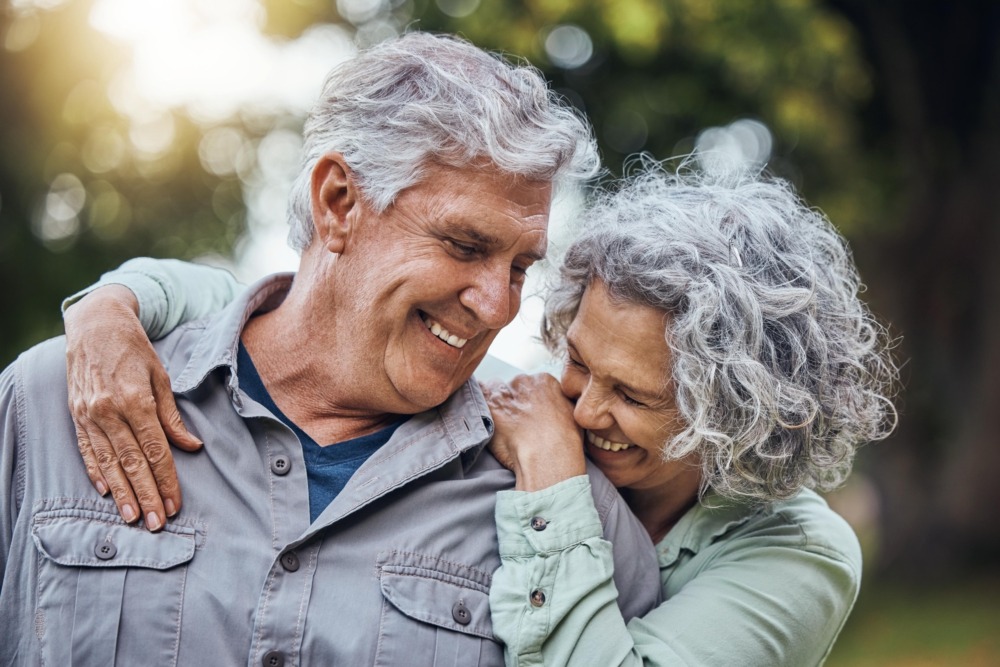 Senior couple outside in the sunshine, laughing and leaning on each other.